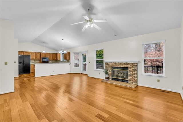 unfurnished living room with ceiling fan with notable chandelier, lofted ceiling, light hardwood / wood-style flooring, and a brick fireplace