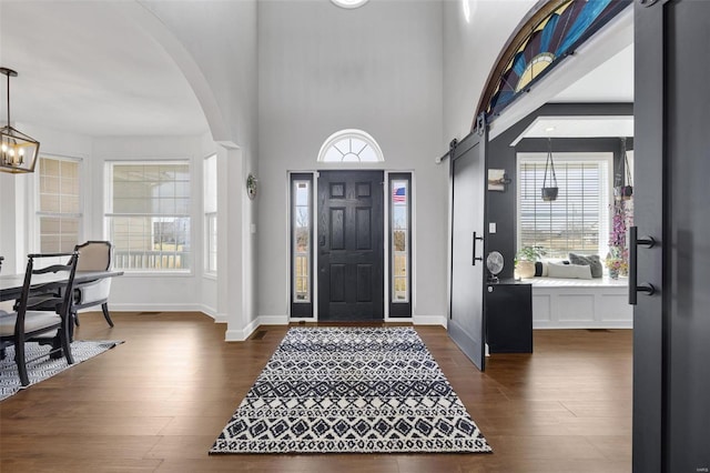 foyer entrance featuring arched walkways, dark wood-style flooring, a notable chandelier, a barn door, and baseboards