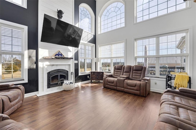 living area with dark wood-type flooring, a towering ceiling, baseboards, and a premium fireplace