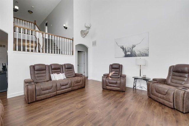 living area featuring baseboards, a high ceiling, arched walkways, and wood finished floors