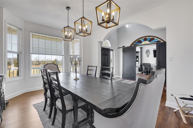 dining room with dark wood-type flooring, arched walkways, baseboards, and an inviting chandelier