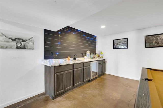 bar featuring beverage cooler, a sink, baseboards, finished concrete flooring, and wet bar