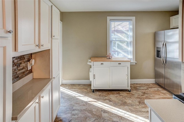 kitchen with stainless steel refrigerator with ice dispenser, white cabinetry, and decorative backsplash