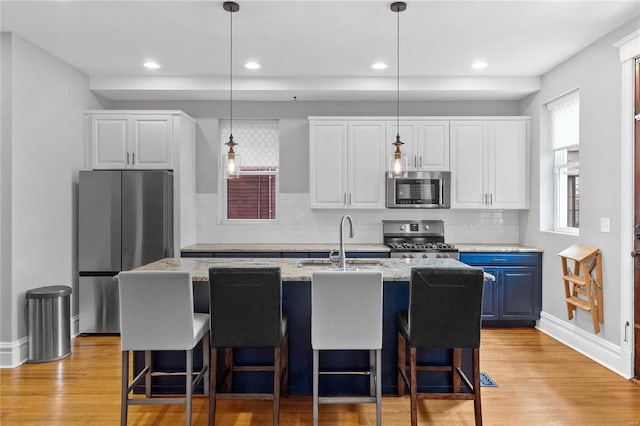 kitchen with appliances with stainless steel finishes, light wood-type flooring, a center island with sink, and white cabinetry