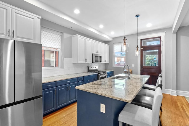 kitchen with blue cabinetry, white cabinetry, sink, stainless steel appliances, and an island with sink