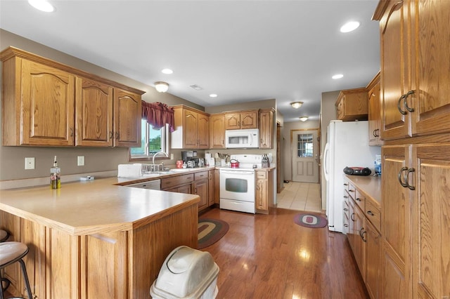 kitchen with sink, kitchen peninsula, a kitchen bar, hardwood / wood-style floors, and white appliances