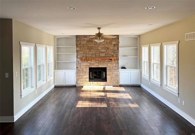 unfurnished living room with built in features, ceiling fan, dark wood-type flooring, and a stone fireplace