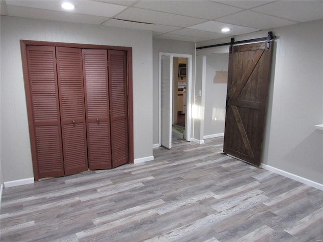 unfurnished bedroom with light wood-type flooring, a paneled ceiling, a barn door, and a closet