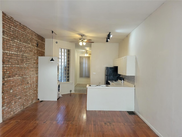 kitchen featuring dark hardwood / wood-style floors, kitchen peninsula, brick wall, pendant lighting, and white cabinetry