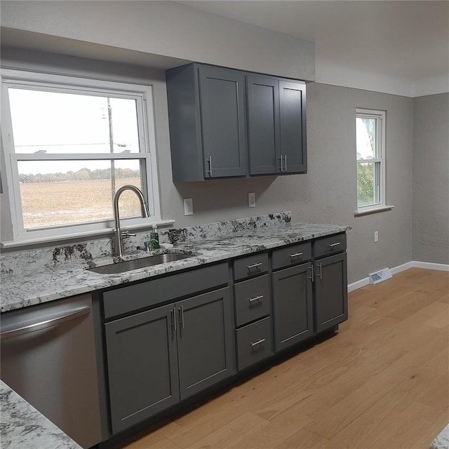 kitchen with light hardwood / wood-style flooring, light stone counters, stainless steel dishwasher, and sink