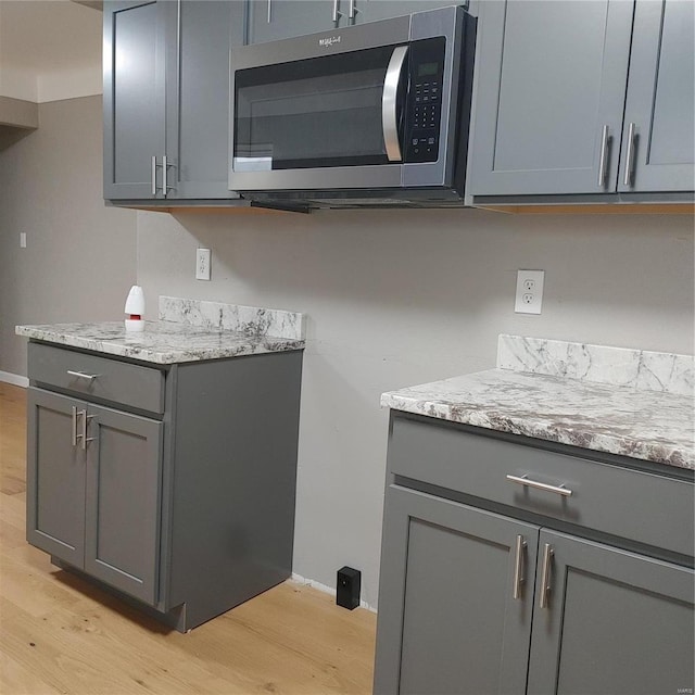 kitchen with gray cabinets, light wood-type flooring, and light stone counters