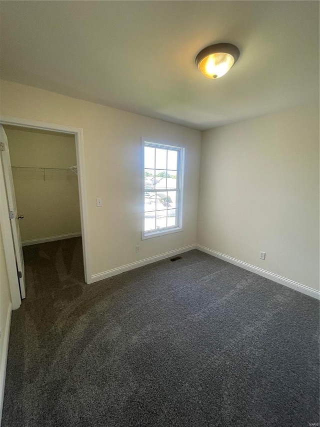 unfurnished bedroom featuring a spacious closet, dark carpet, and a closet