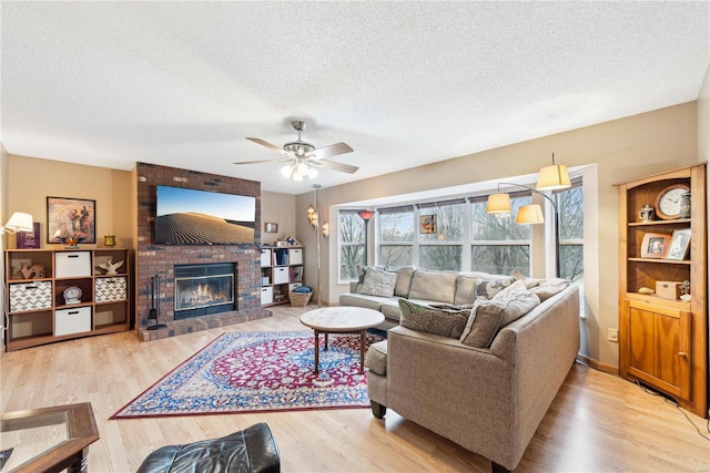 living room with a textured ceiling, ceiling fan, light wood-type flooring, and a fireplace