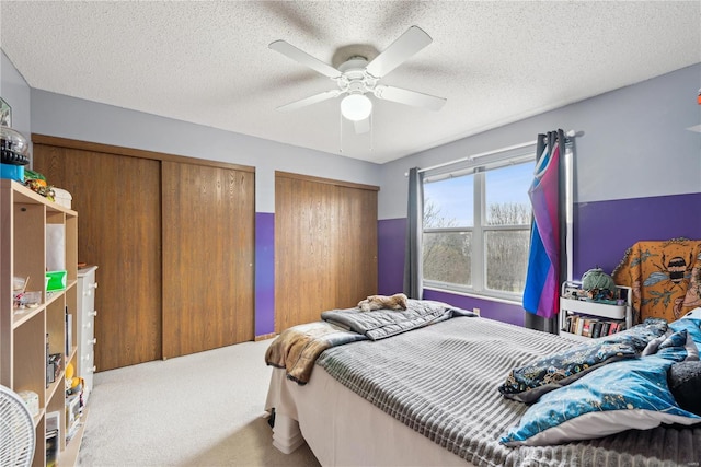 carpeted bedroom with multiple closets, ceiling fan, and a textured ceiling