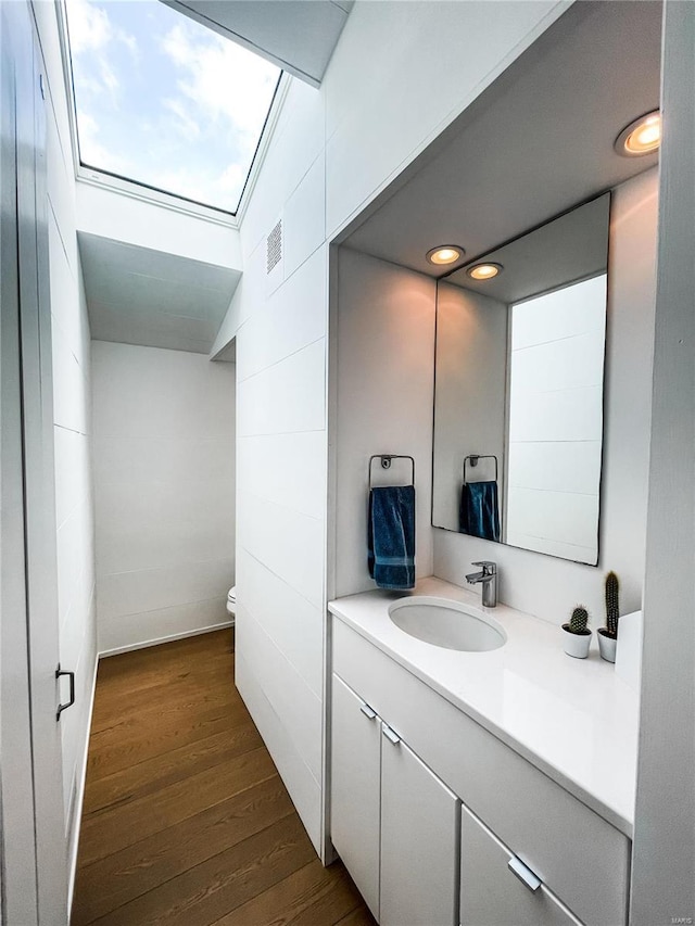 bathroom with hardwood / wood-style flooring, vanity, toilet, and vaulted ceiling