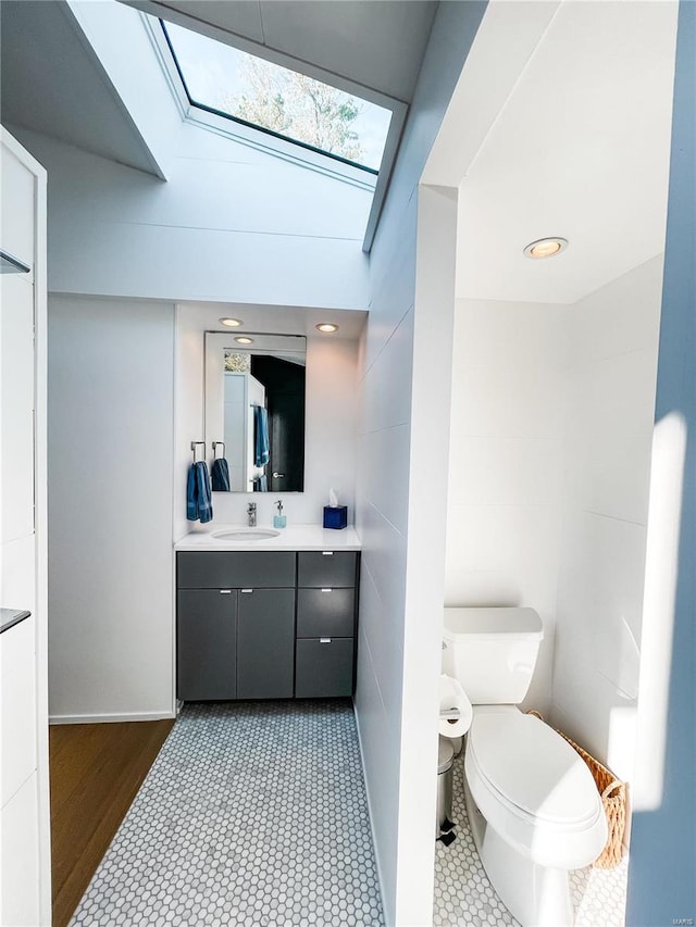 bathroom featuring tile walls, vanity, lofted ceiling with skylight, hardwood / wood-style floors, and toilet