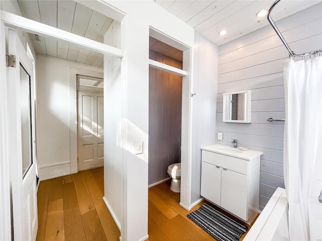 full bathroom with vanity, wooden walls, hardwood / wood-style floors, toilet, and shower / bath combo with shower curtain