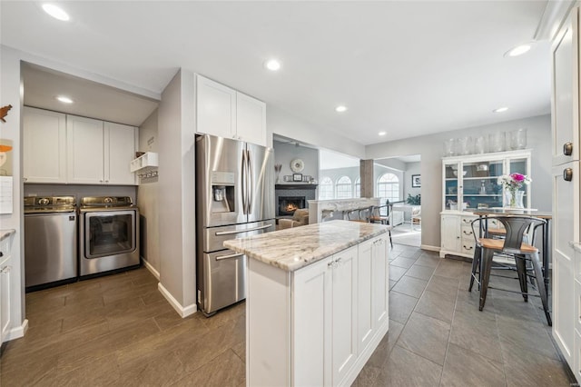 kitchen with stainless steel refrigerator with ice dispenser, open floor plan, a lit fireplace, white cabinets, and washing machine and clothes dryer