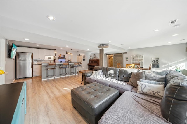 living room featuring a barn door, visible vents, recessed lighting, and light wood-style floors