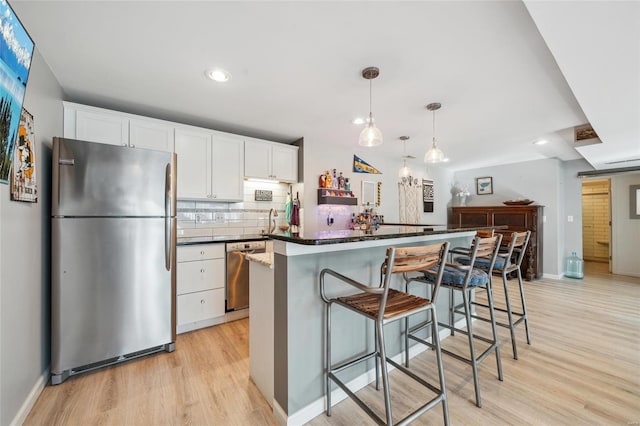 kitchen with white cabinetry, light wood-style flooring, backsplash, and stainless steel appliances