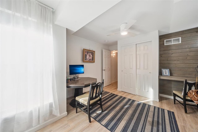 office area featuring light wood finished floors, visible vents, wood walls, and ceiling fan