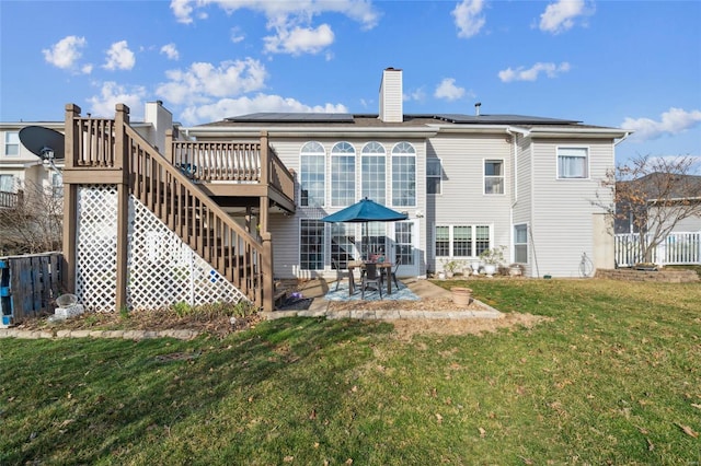 back of house with stairs, roof mounted solar panels, a chimney, a yard, and a patio