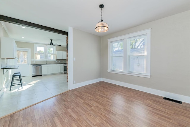 unfurnished dining area featuring light wood-type flooring, a wealth of natural light, and beam ceiling