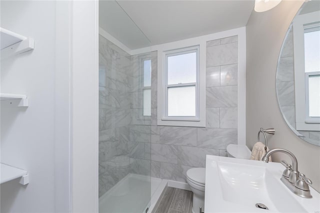 bathroom with a tile shower, wood-type flooring, sink, and toilet