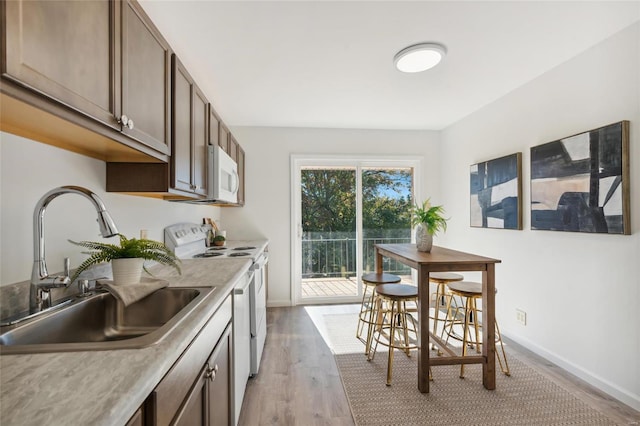 kitchen featuring dark brown cabinetry, sink, white appliances, and light wood-type flooring