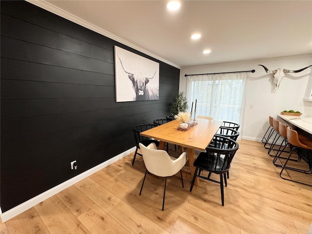 dining room featuring light wood-type flooring, crown molding, and wooden walls