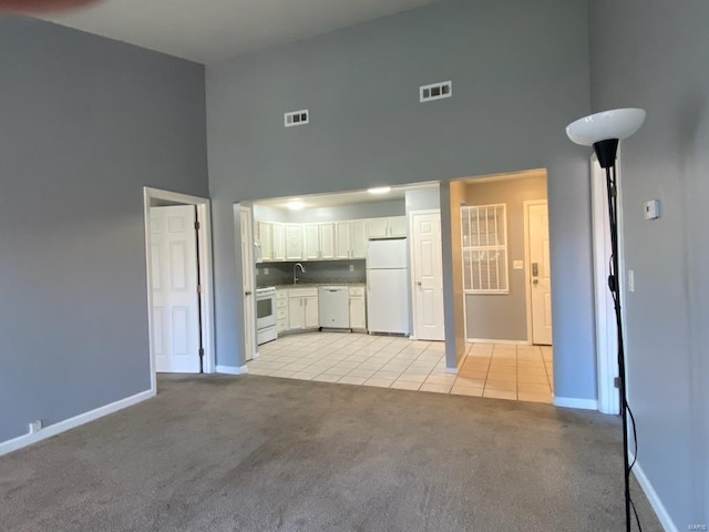 unfurnished living room with light carpet, sink, and a towering ceiling