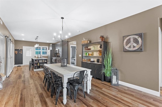 dining area with sink, a notable chandelier, and light hardwood / wood-style flooring