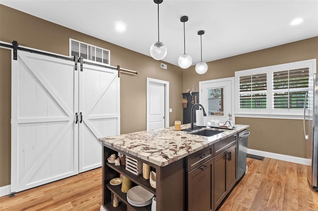 kitchen with light stone countertops, sink, light wood-type flooring, a barn door, and pendant lighting