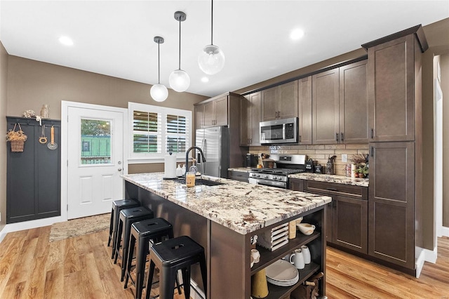 kitchen with hanging light fixtures, dark brown cabinets, an island with sink, light hardwood / wood-style flooring, and stainless steel appliances