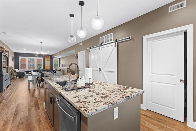 kitchen with a kitchen island with sink, light hardwood / wood-style flooring, a barn door, decorative light fixtures, and stainless steel dishwasher