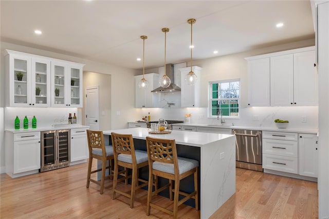 kitchen featuring white cabinetry, sink, beverage cooler, stainless steel dishwasher, and wall chimney range hood