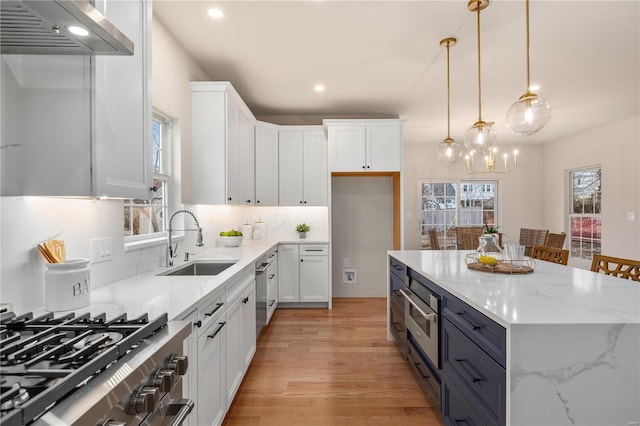 kitchen featuring decorative light fixtures, white cabinetry, sink, stainless steel appliances, and wall chimney exhaust hood