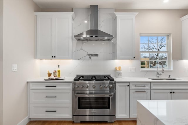 kitchen with wall chimney exhaust hood, sink, white cabinetry, stainless steel stove, and light stone countertops