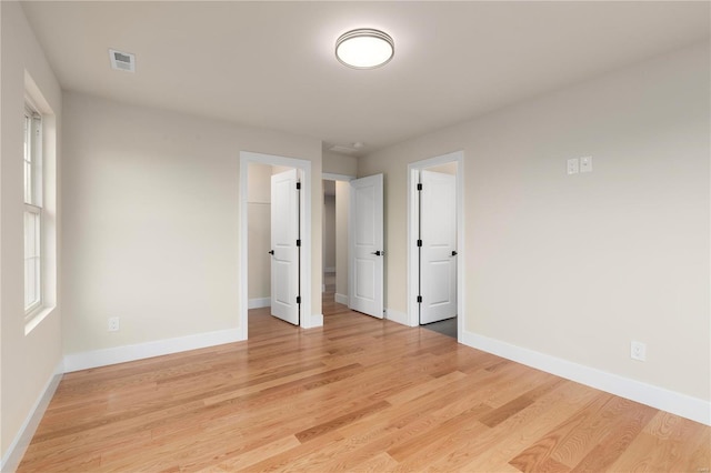 unfurnished bedroom with multiple windows, a spacious closet, and light wood-type flooring