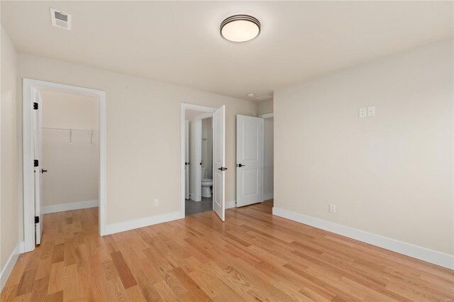 unfurnished bedroom with a spacious closet, ensuite bath, a closet, and light wood-type flooring