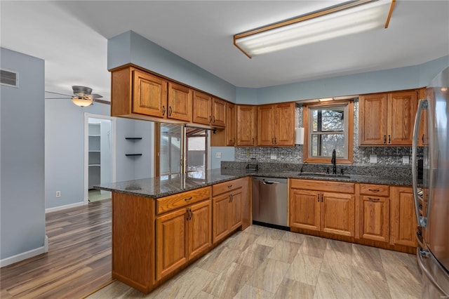 kitchen featuring sink, ceiling fan, dark stone countertops, appliances with stainless steel finishes, and kitchen peninsula