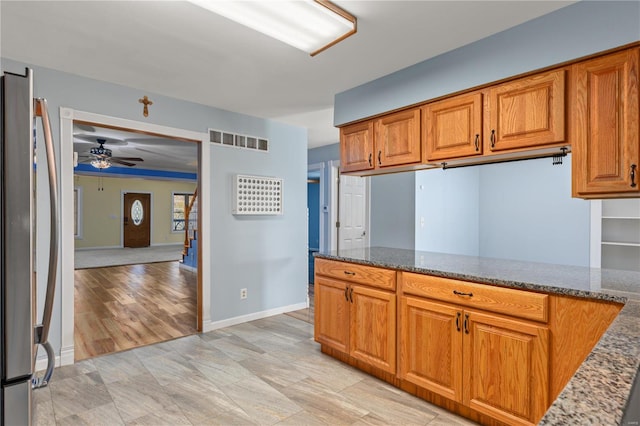 kitchen featuring ceiling fan, light hardwood / wood-style floors, stainless steel refrigerator, and dark stone counters