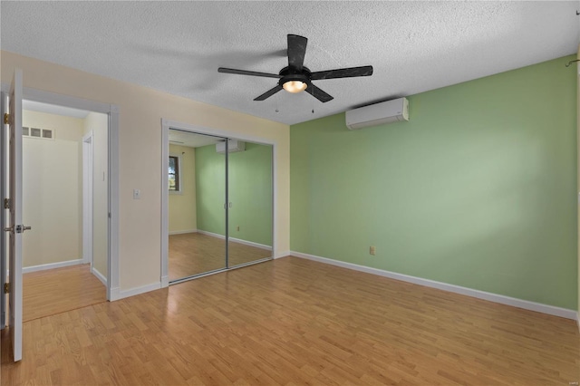 unfurnished bedroom with ceiling fan, a wall unit AC, light hardwood / wood-style floors, a textured ceiling, and a closet