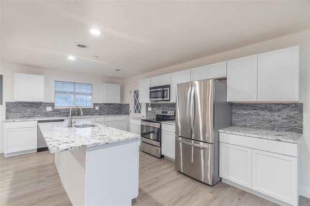 kitchen featuring appliances with stainless steel finishes, sink, white cabinets, a kitchen island with sink, and light hardwood / wood-style flooring