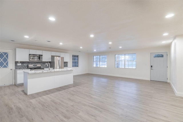 kitchen with light hardwood / wood-style flooring, a kitchen island with sink, stainless steel appliances, tasteful backsplash, and white cabinets