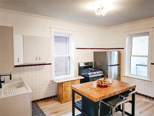 kitchen with white cabinets, stainless steel appliances, sink, and tile walls