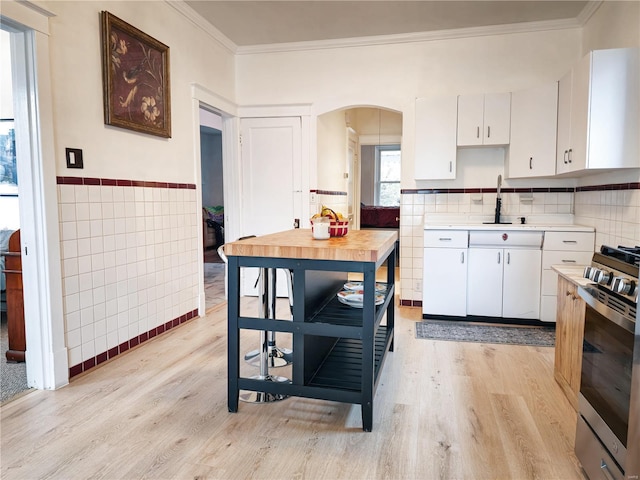 kitchen featuring white cabinets, tile walls, stainless steel gas stove, crown molding, and light hardwood / wood-style flooring