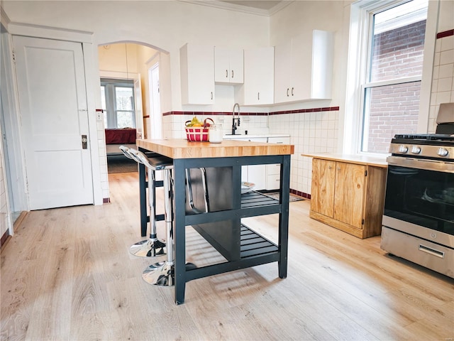 kitchen featuring white cabinetry, stainless steel stove, wood counters, and light hardwood / wood-style flooring