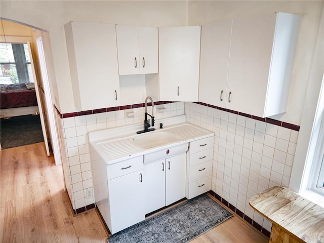 kitchen featuring light wood-type flooring, tile walls, sink, and white cabinets