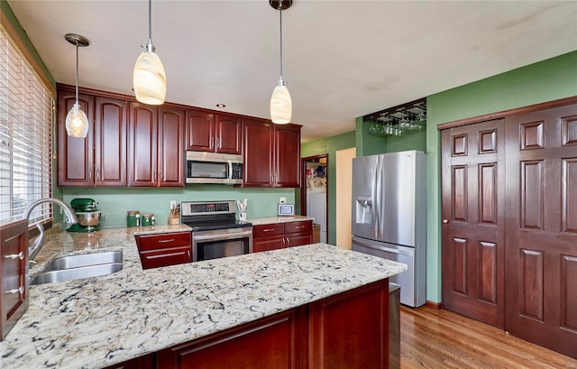 kitchen with sink, hanging light fixtures, light wood-type flooring, light stone counters, and stainless steel appliances